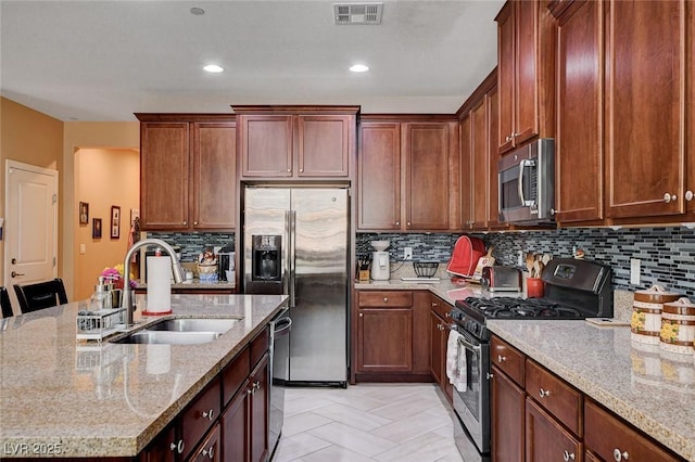 kitchen featuring appliances with stainless steel finishes, a sink, light stone countertops, an island with sink, and backsplash