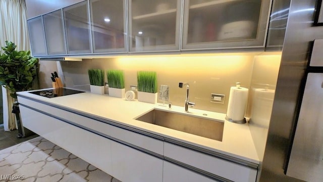 kitchen featuring a sink, black electric cooktop, white cabinetry, light countertops, and glass insert cabinets