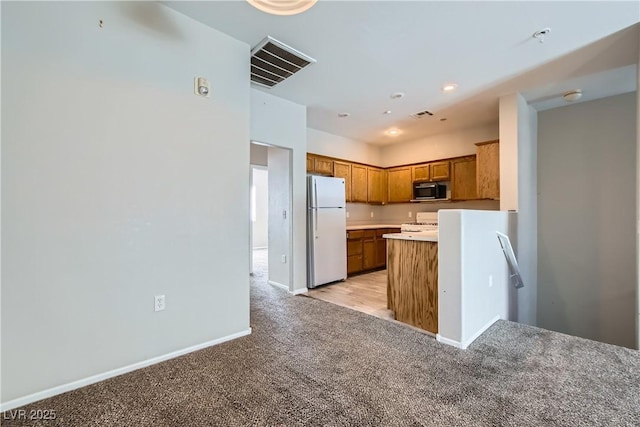 5915 Nuevo Leon St Unit 8, North Las Vegas, NV 89031 - kitchen with freestanding refrigerator, black microwave, light carpet, brown cabinetry, and range