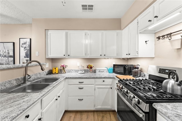 kitchen with gas stove, a sink, and white cabinets