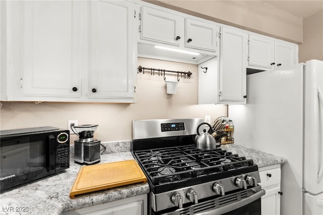 kitchen with stainless steel range with gas stovetop, black microwave, white cabinetry, light countertops, and freestanding refrigerator