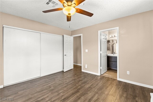 unfurnished bedroom with dark wood-type flooring, a closet, baseboards, a textured ceiling, and connected bathroom