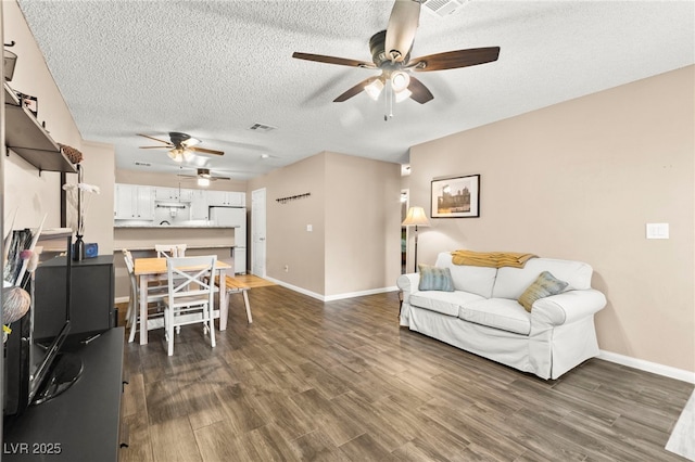 living area featuring ceiling fan, a textured ceiling, baseboards, and dark wood-style flooring