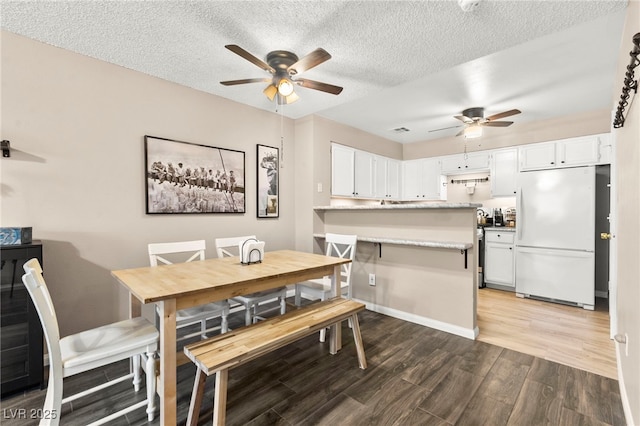 dining area featuring a ceiling fan, light wood finished floors, a textured ceiling, and baseboards