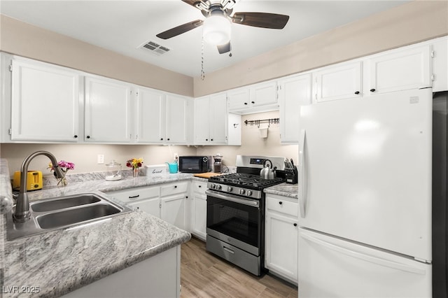 kitchen with freestanding refrigerator, stainless steel range with gas stovetop, a sink, black microwave, and white cabinets