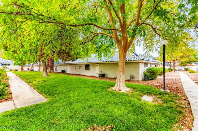 back of house with stucco siding, a yard, central AC, and a tile roof
