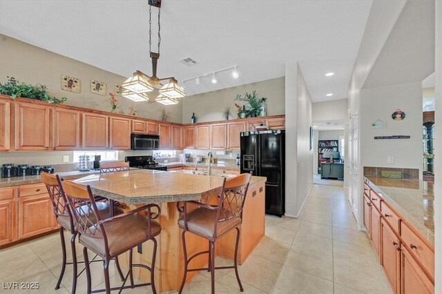 8208 Flowing Rapids Ct, Las Vegas, NV 89131 - kitchen with stainless steel microwave, black fridge with ice dispenser, range, a center island with sink, and light tile patterned floors