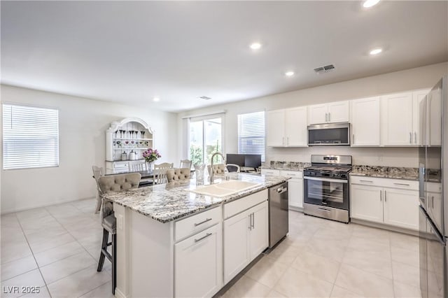 kitchen featuring appliances with stainless steel finishes, a sink, white cabinetry, a kitchen bar, and a center island with sink