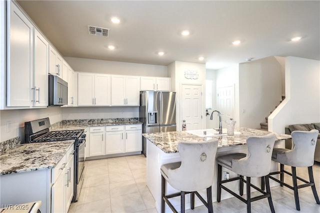 kitchen with stainless steel appliances, a sink, a breakfast bar, light stone countertops, and white cabinetry