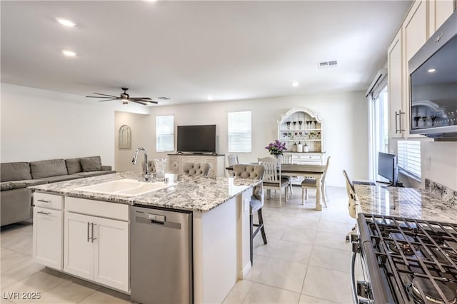 kitchen featuring stainless steel appliances, a sink, open floor plan, white cabinetry, and plenty of natural light
