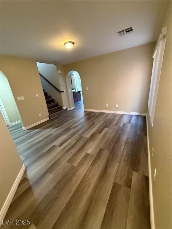 unfurnished living room with arched walkways, wood finished floors, stairway, and baseboards
