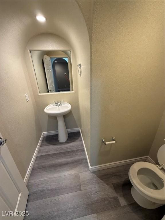 half bath with wood finished floors, baseboards, and toilet
