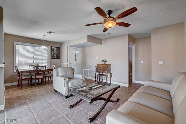 living area with ceiling fan, a textured ceiling, and baseboards