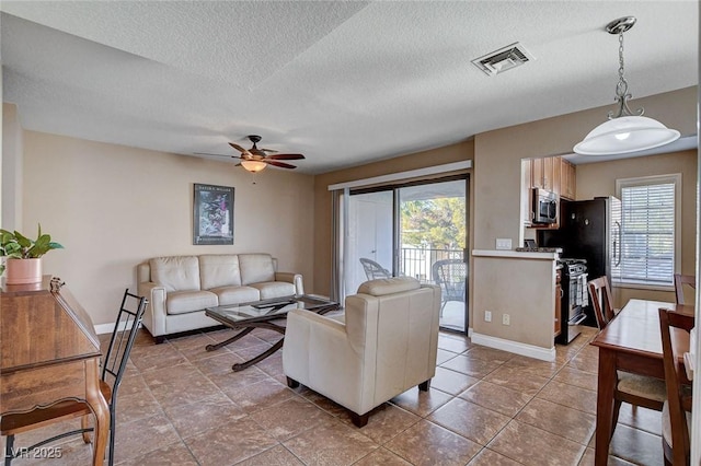 living room featuring healthy amount of natural light, a ceiling fan, baseboards, and a textured ceiling