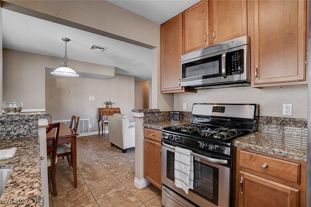 kitchen with appliances with stainless steel finishes, light tile patterned floors, dark stone countertops, and pendant lighting