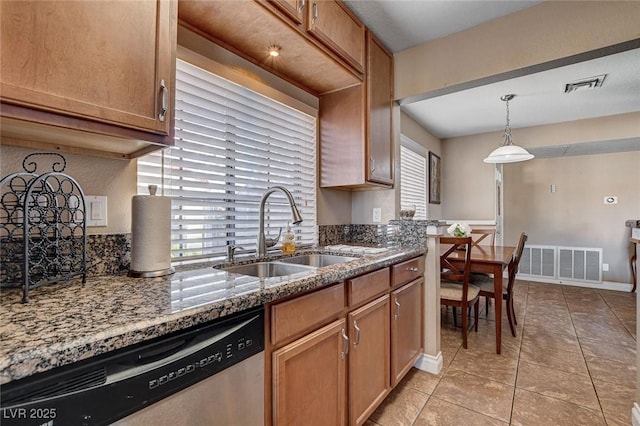kitchen with dishwasher, a sink, dark stone counters, light tile patterned flooring, and hanging light fixtures