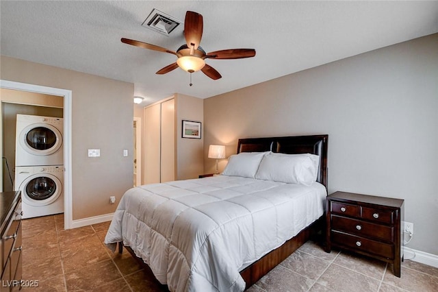 bedroom featuring stacked washer and clothes dryer, baseboards, tile patterned floors, a closet, and ceiling fan
