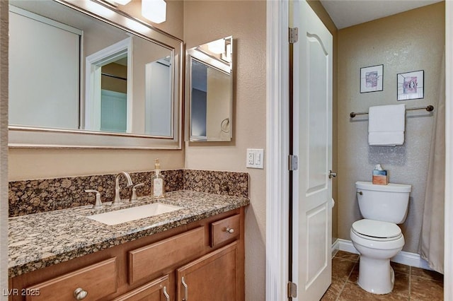 bathroom with toilet, vanity, tile patterned floors, baseboards, and a textured wall