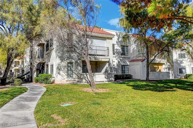 view of front of property featuring a balcony, a front lawn, stucco siding, stairway, and a tiled roof