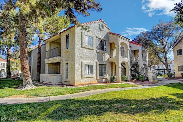 view of front facade with stucco siding, a front lawn, a balcony, a tiled roof, and stairs