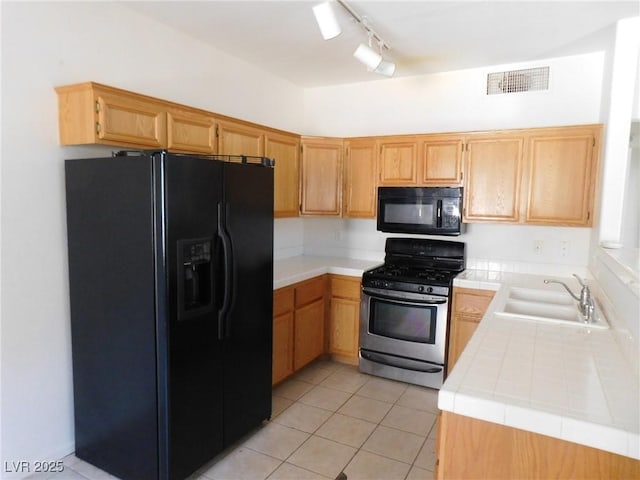 kitchen with black appliances, a sink, tile counters, rail lighting, and light tile patterned flooring