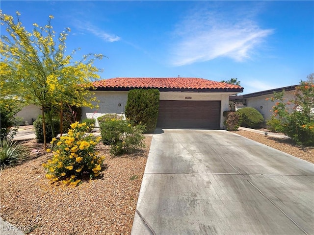 mediterranean / spanish-style house with stucco siding, an attached garage, a tile roof, and concrete driveway