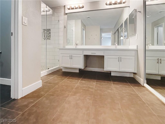 bathroom with a shower stall, tile patterned flooring, double vanity, and baseboards