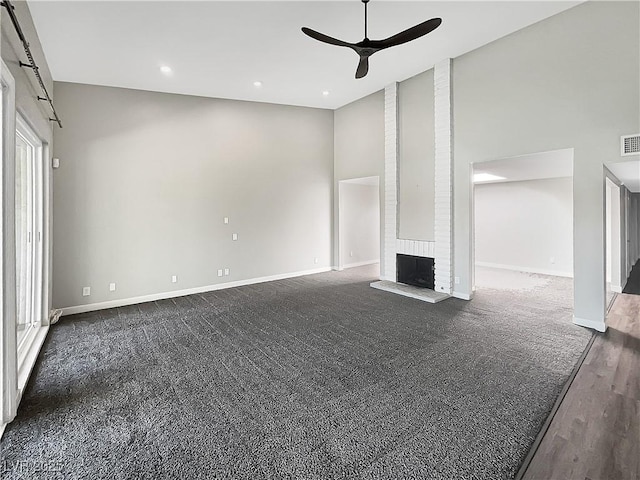 unfurnished living room featuring a ceiling fan, baseboards, dark colored carpet, a fireplace, and a towering ceiling