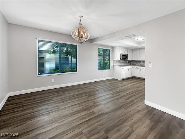 unfurnished living room with a chandelier, baseboards, dark wood finished floors, and a tray ceiling