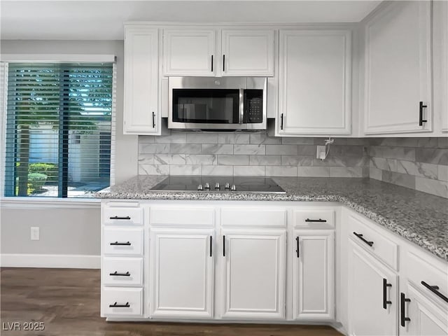 kitchen with stainless steel microwave, black electric stovetop, baseboards, tasteful backsplash, and white cabinetry