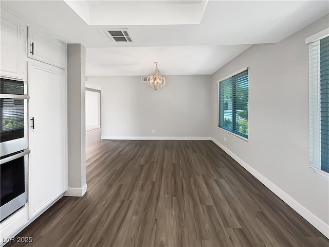 unfurnished dining area featuring dark wood-style flooring, a chandelier, and baseboards