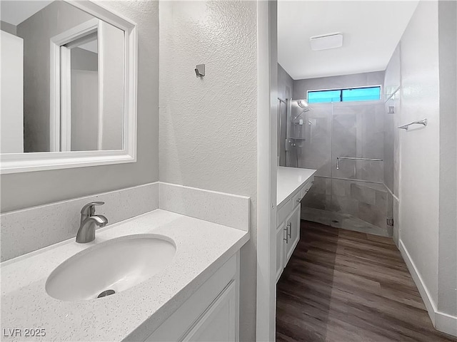 full bath with vanity, a stall shower, wood finished floors, and a textured wall