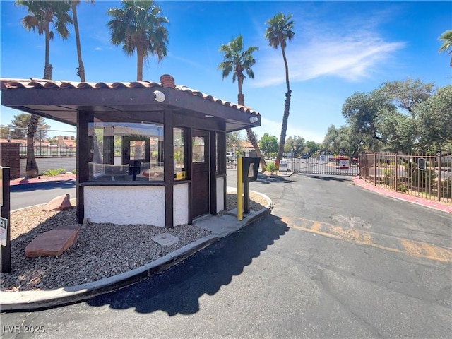 view of asphalt road featuring a gate, a gated entry, and curbs