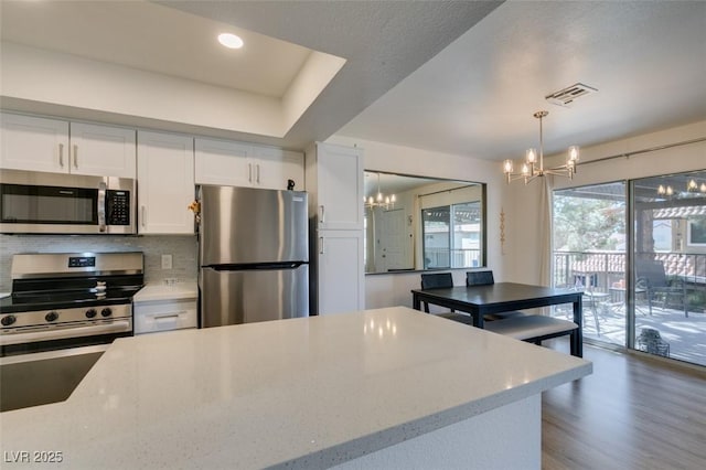 718 Nectarine Ct, Henderson, NV 89014 - kitchen featuring stainless steel appliances, a chandelier, white cabinets, decorative light fixtures, and light stone counters