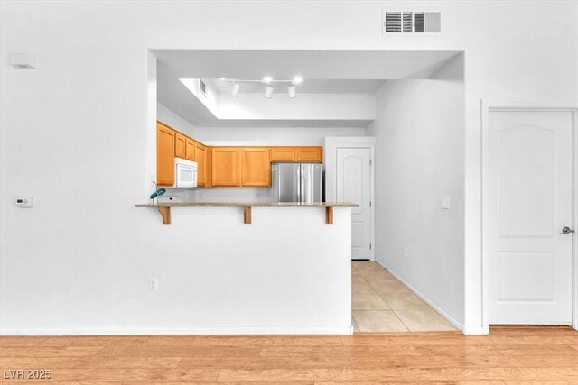 8985 S Durango Dr Unit 1110, Las Vegas, NV 89113 - kitchen featuring freestanding refrigerator, white microwave, a breakfast bar, a peninsula, and stone counters