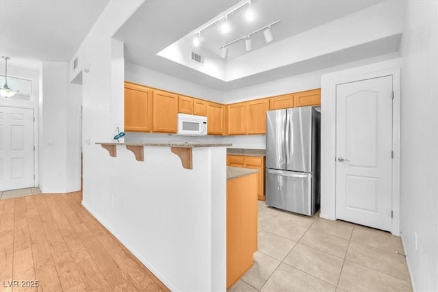 8985 S Durango Dr Unit 1110, Las Vegas, NV 89113 - kitchen featuring freestanding refrigerator, white microwave, a kitchen breakfast bar, a peninsula, and a raised ceiling