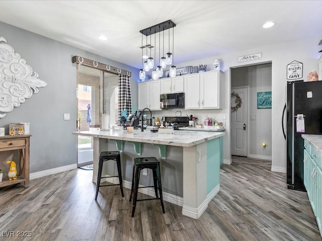 kitchen with black appliances, a sink, wood finished floors, a breakfast bar, and white cabinetry