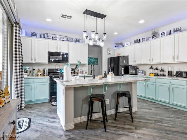 kitchen featuring black appliances, wood finished floors, a kitchen island with sink, pendant lighting, and a breakfast bar