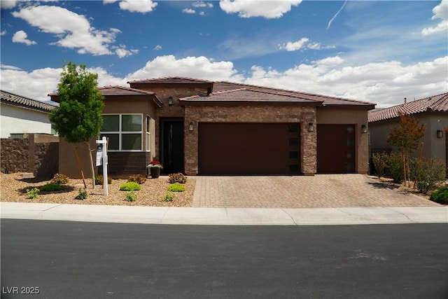 view of front of property featuring an attached garage, decorative driveway, stone siding, and stucco siding