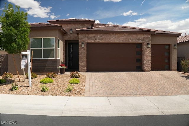 prairie-style house with an attached garage, decorative driveway, stucco siding, and a tile roof