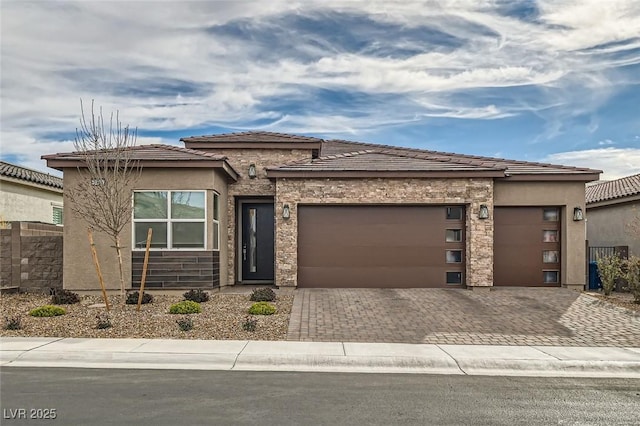 prairie-style house with an attached garage, driveway, and stone siding