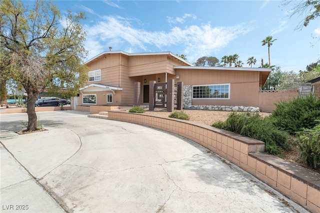 view of front of home featuring curved driveway, stone siding, and fence