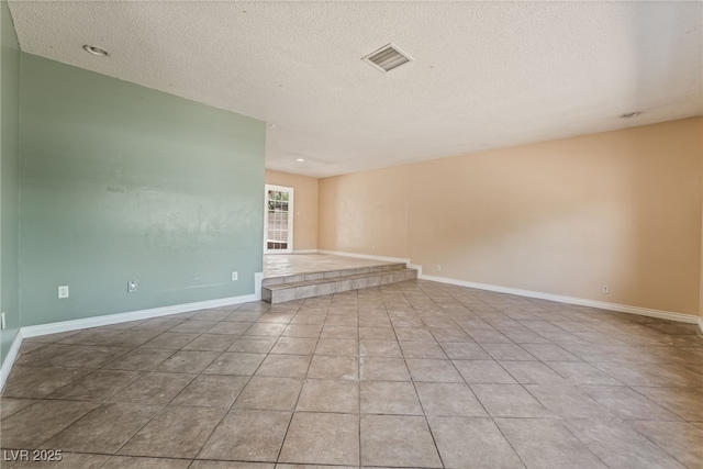 empty room with a textured ceiling, baseboards, and tile patterned flooring