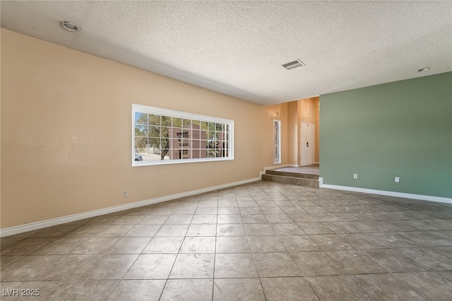 tiled spare room featuring a textured ceiling and baseboards