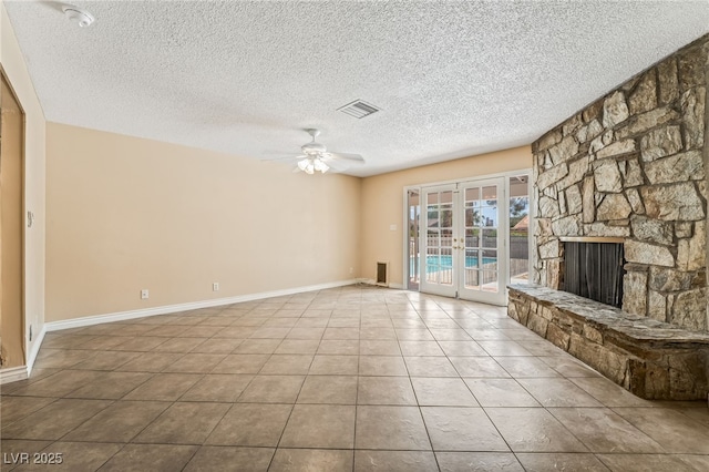 unfurnished living room with french doors, a ceiling fan, a textured ceiling, tile patterned floors, and a stone fireplace