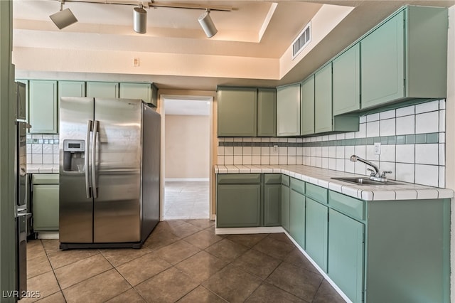 kitchen with stainless steel fridge with ice dispenser, a sink, green cabinets, tile counters, and track lighting