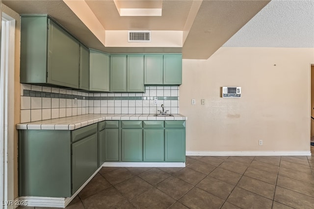 kitchen featuring green cabinetry, tile countertops, decorative backsplash, dark tile patterned flooring, and a sink