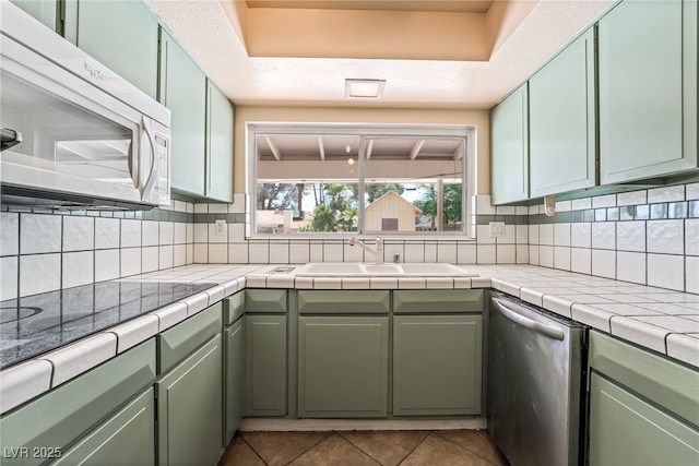 kitchen featuring white microwave, a sink, stainless steel dishwasher, green cabinetry, and tile patterned flooring