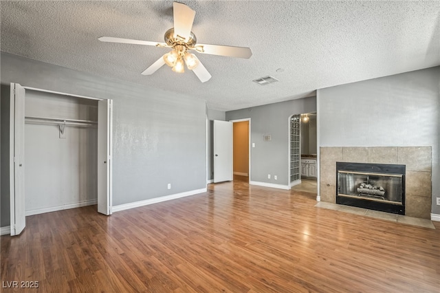 unfurnished living room with wood finished floors, a ceiling fan, a textured ceiling, a fireplace, and baseboards