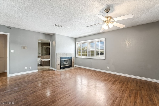 unfurnished living room featuring arched walkways, wood finished floors, ceiling fan, a textured ceiling, and baseboards